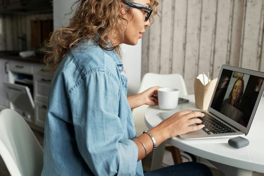 Une femme souriante, les yeux mi-clos, assise devant un ordinateur portable en pl;en de tchat avec une autre femme, explorant sa sexualité